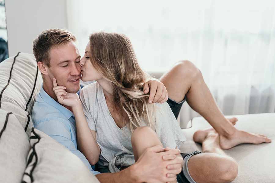 unas parejas están en el sofa y la mujer dando un beso a un hombre. 