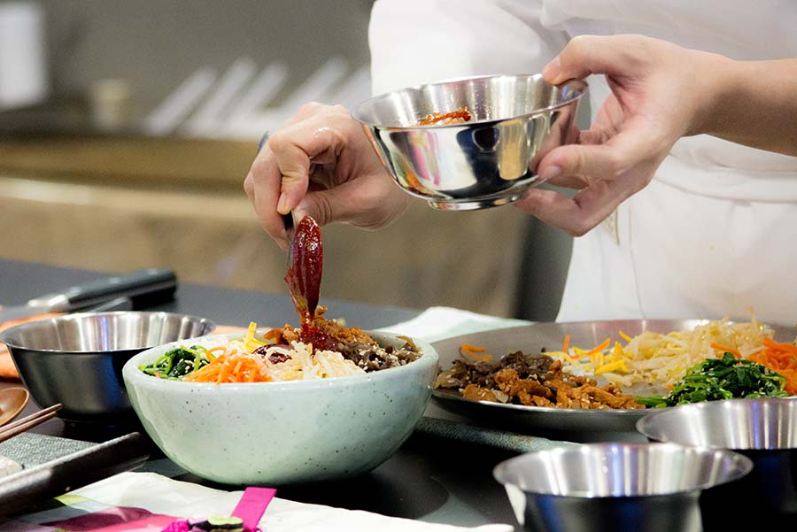 Está preparando la comida coreana bibimbap, está poniendo una salsa gochujang