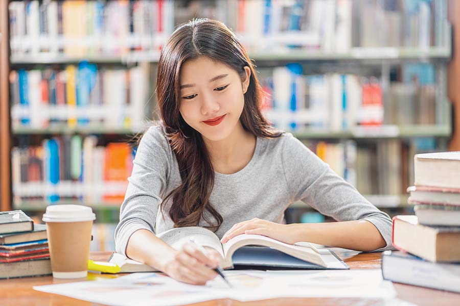 Una mujer está estudiando mientras lee un libro en la biblioteca.