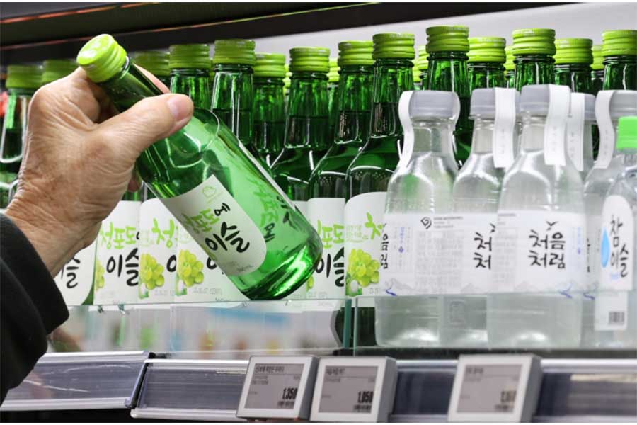 Se ve una mano sacando una botella de soju del refrigerador.
