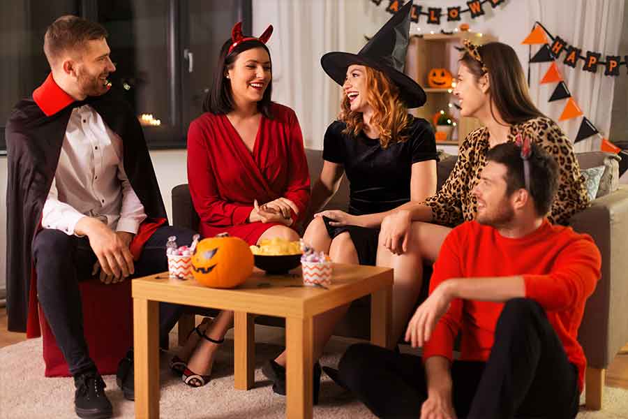 Tres mujeres y dos hombres están en una casa, vestidos con disfraces de Halloween y celebrando una fiesta.