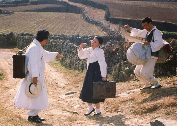 En un campo, dos hombres y una mujer con hanbok.
