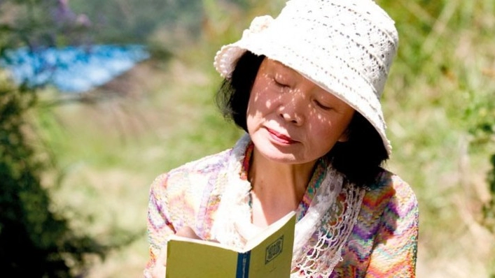 Una mujer con un sombrero blanco está leyendo un poemario.
